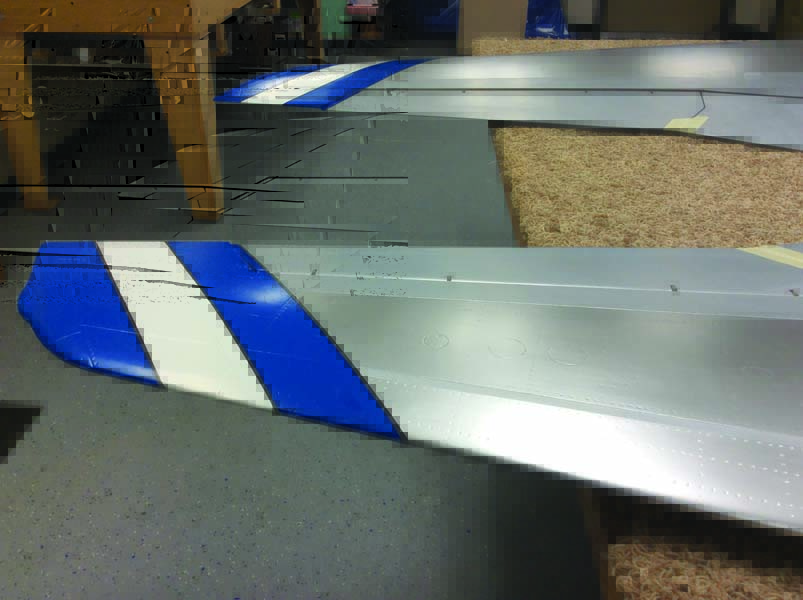 The wingtip stripes are complete: white, then blue, and the final thin black stripes. On the leading edge and center of the wing, Matt applied platinum paint to give the finish a bright aluminum look.