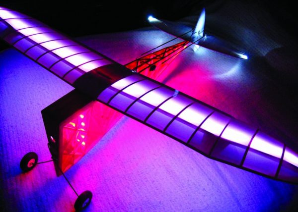 This scratch-built balsa plane is the Wedgy, featured in Model Airplane News November, 1940. The V-shaped fuselage is covered with transparent red and has solid white strip LEDs shining downward. The wing is white on the top and clear on the bottom. It has programmable LEDs shining upward in the wing.